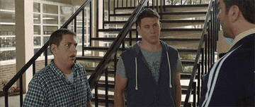 Jonah Hill, Channing Tatum, and Dave Franco stand in front of stairs, talking in a scene from a film. Jonah looks surprised, Channing looks serious