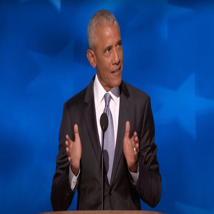 Barack Obama stands at a podium, gesturing with both hands, giving a speech against a blue backdrop adorned with star patterns