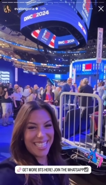 Eva Longoria smiles for a selfie at the DNC 2024 event. The background shows a stage, cameras, and people. Text on the image