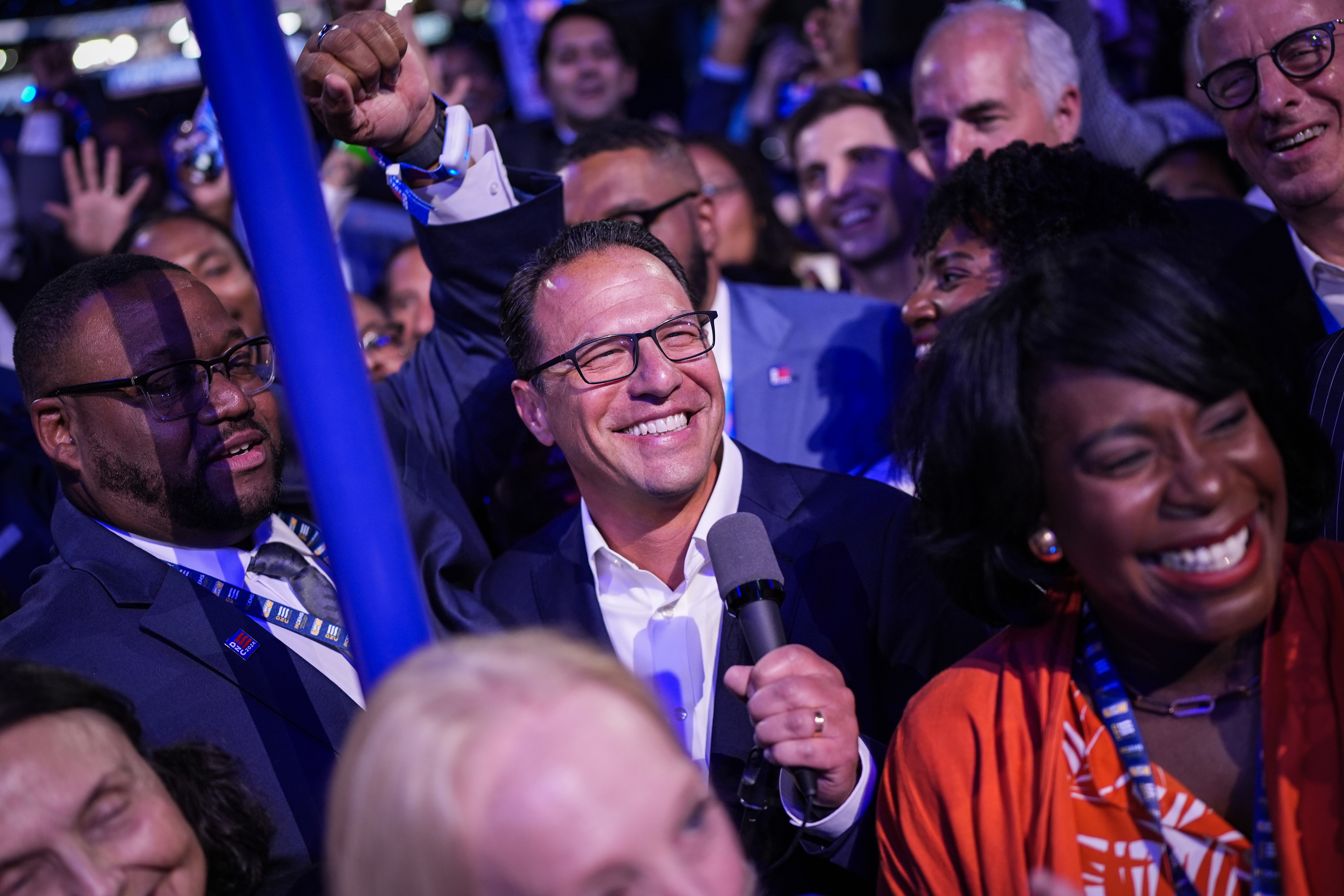 A joyful crowd celebrates as Josh Shapiro smiles and holds a microphone amidst his supporters
