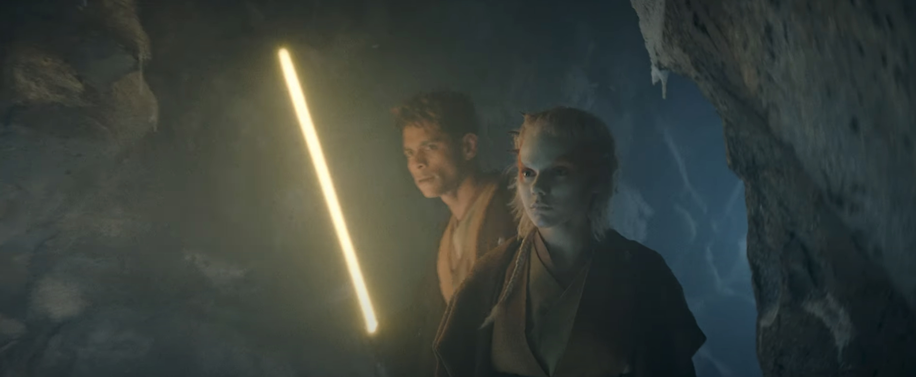Jedi in a dimly lit cave, holding lightsabers, from a scene in the Star Wars series