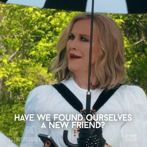 Moira Rose from Schitt's Creek, wearing a stylish outfit with gloves, holds an umbrella and says, "HAVE WE FOUND OURSELVES A NEW FRIEND?"