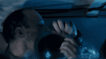A man with a shaved head urgently taps a small screen underwater, surrounded by a blue-lit environment