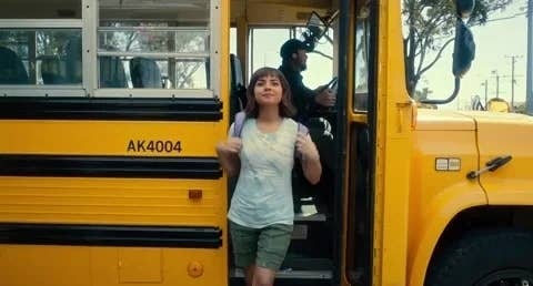 A woman with a backpack exits a school bus as the driver looks on