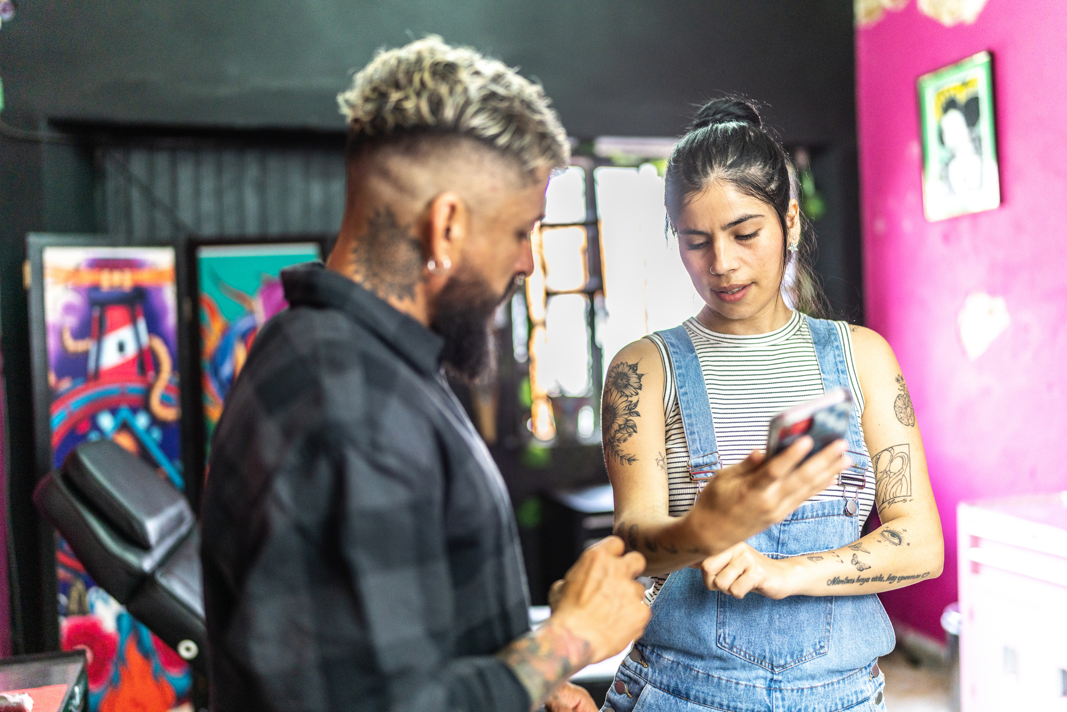 Two people in a tattoo studio discussing a tattoo design on one of their phones