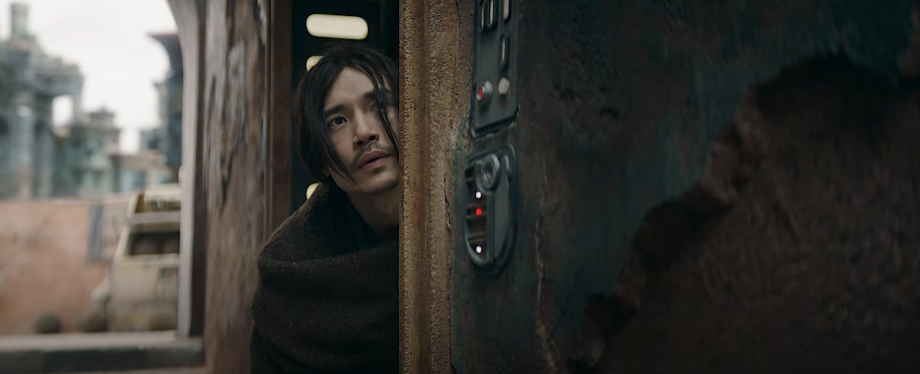 Person peeks anxiously from behind a wall in a dystopian setting with run-down structures visible in the background