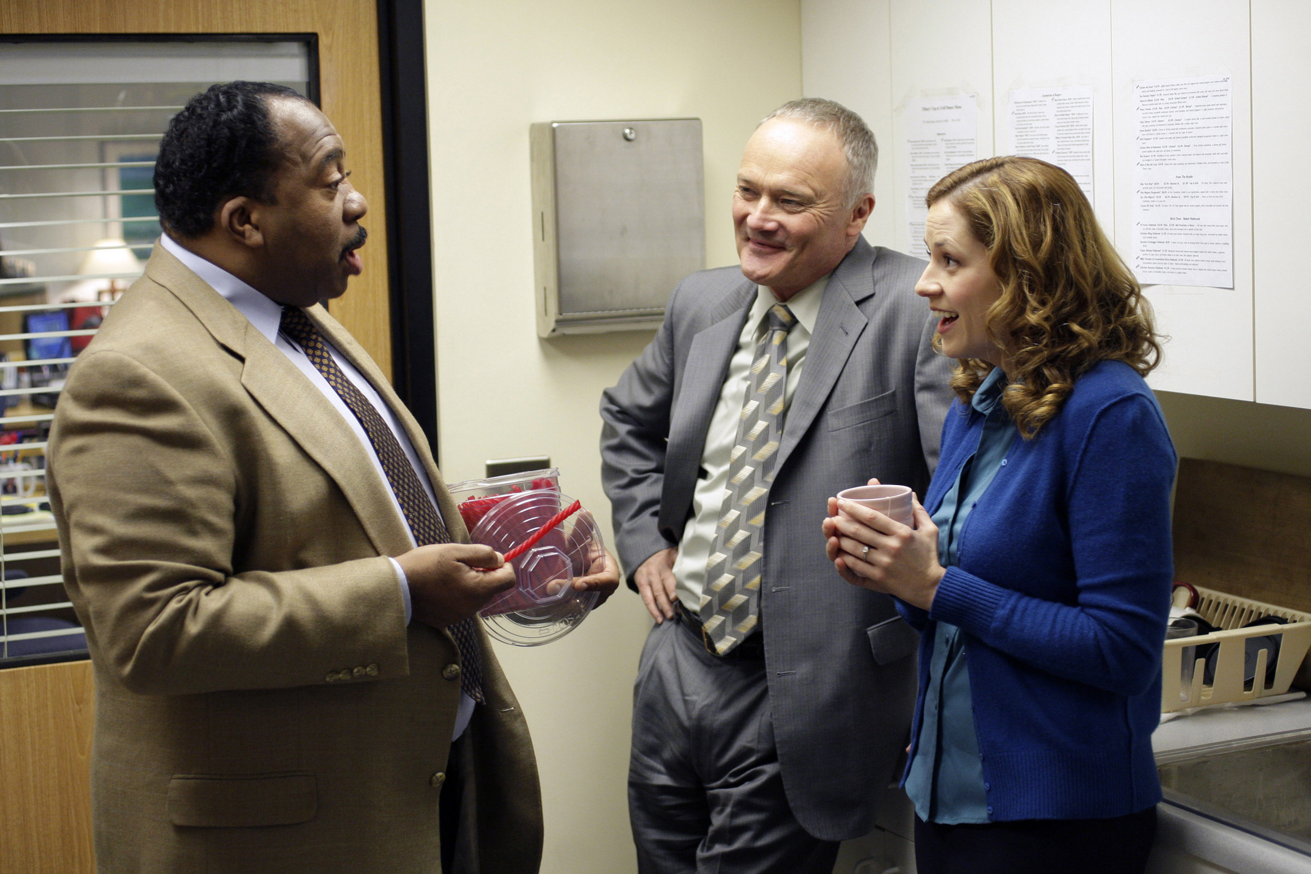 Stanley Hudson, Creed Bratton, and Pam Beesly from "The Office" talking in the break room while holding coffee and Tupperware