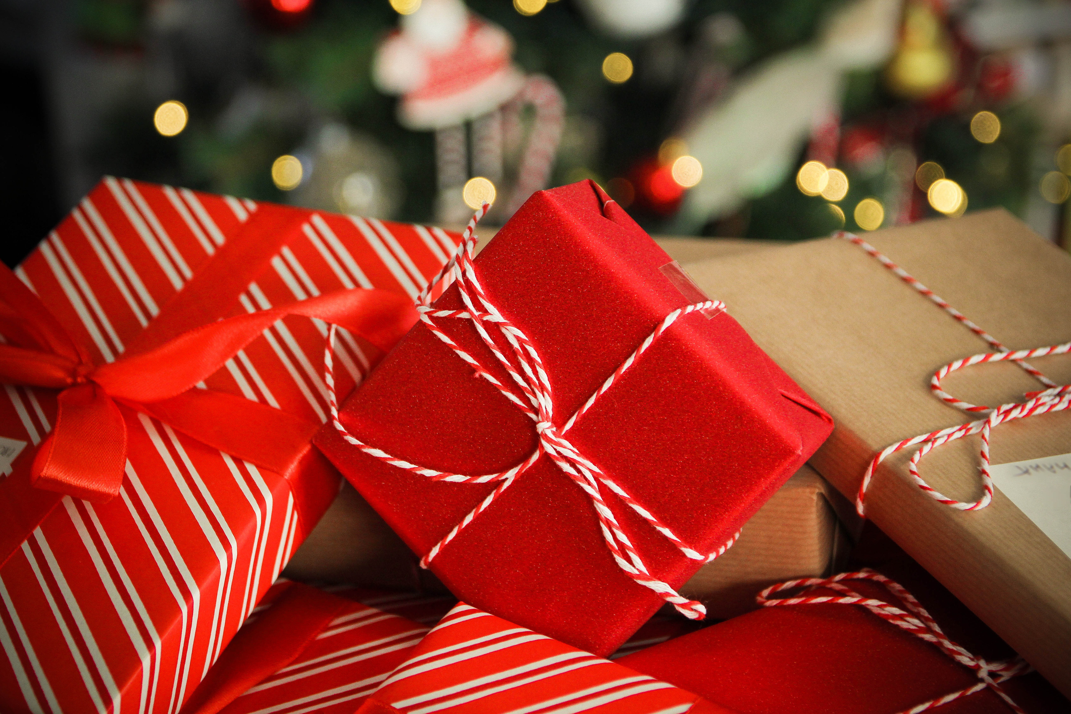 A stack of wrapped presents with ribbons placed in front of a decorated Christmas tree