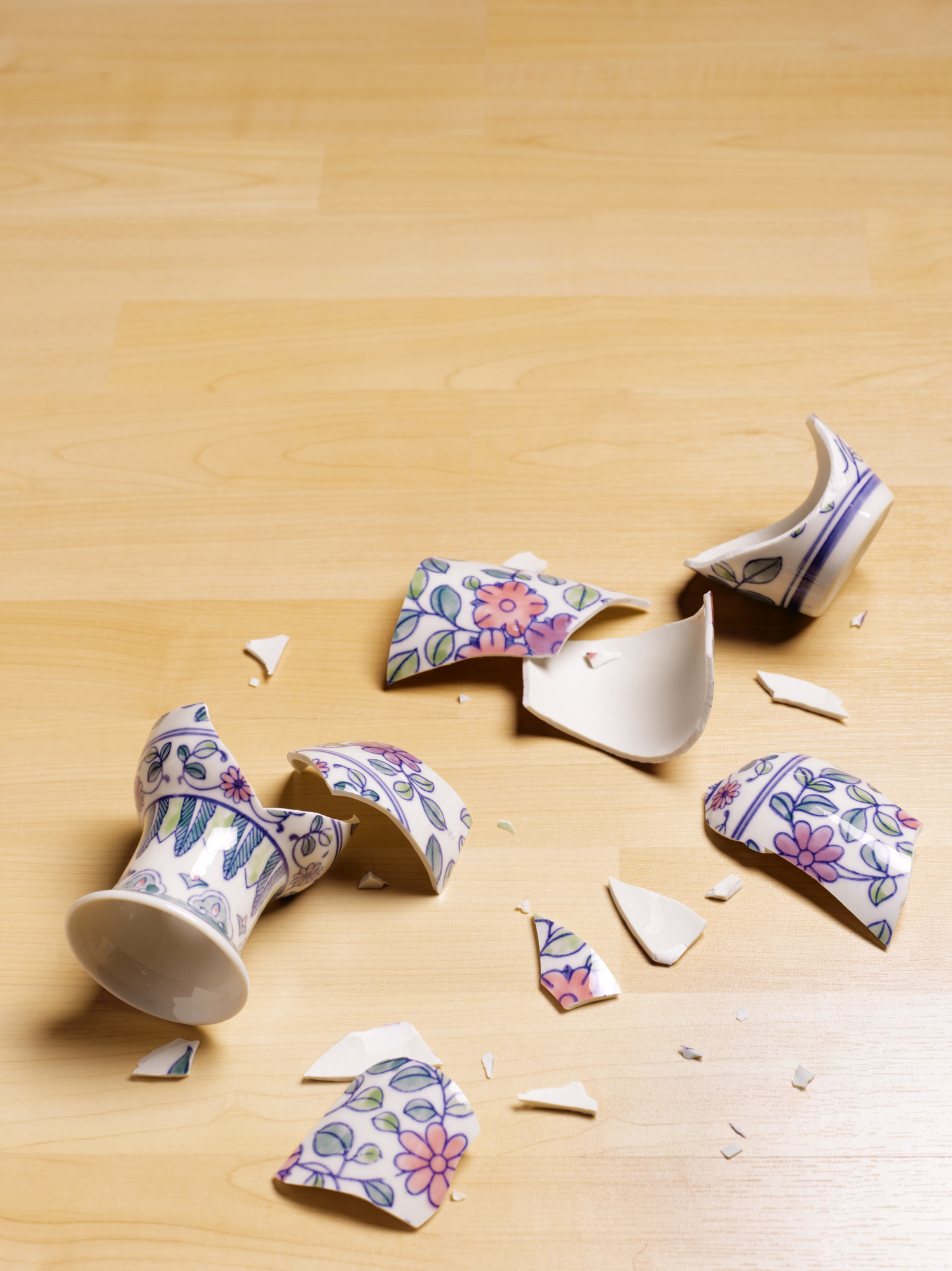 Broken ceramic cup with floral patterns scattered on wooden floor
