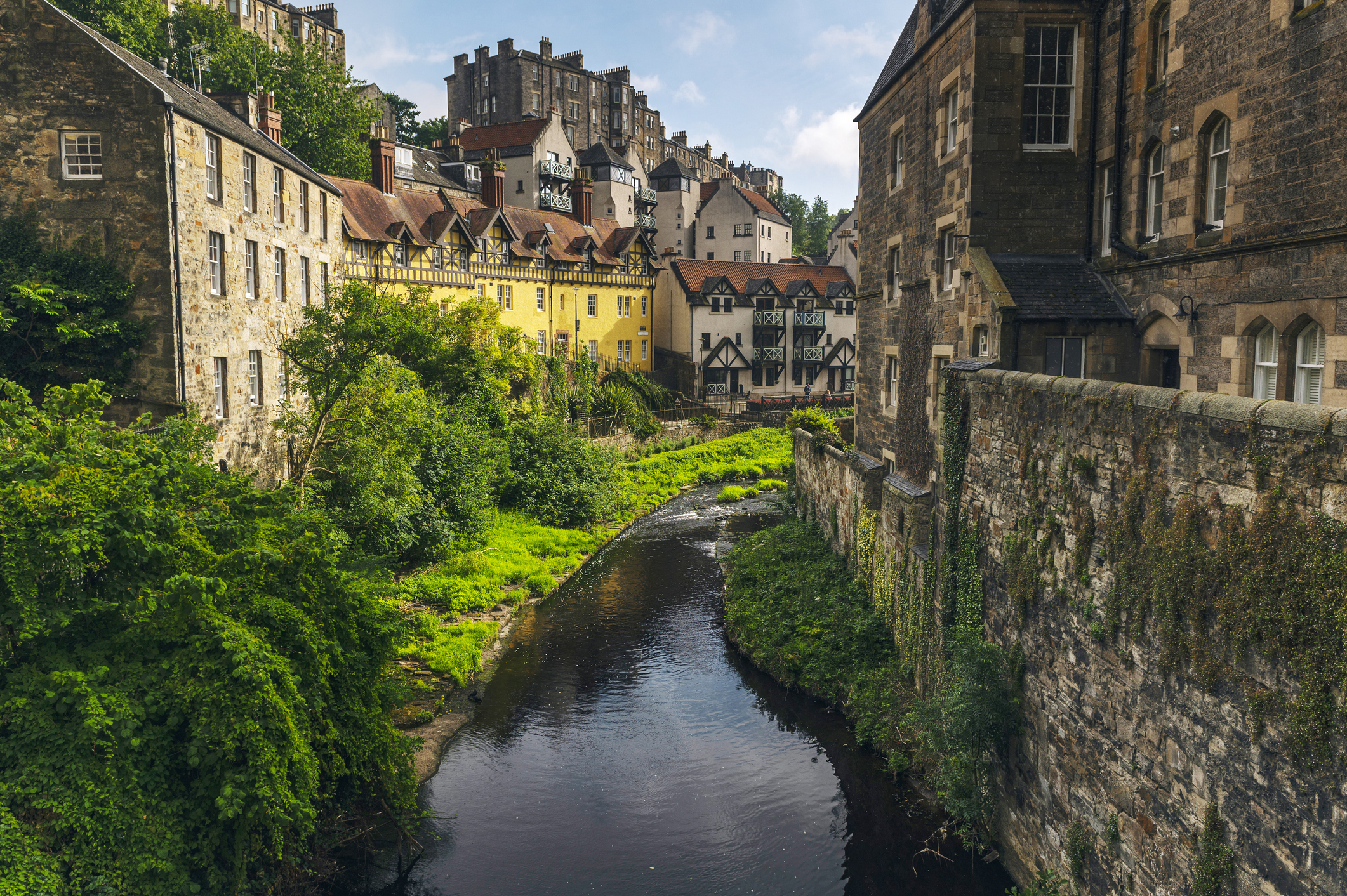 A charming view of a historic village with a narrow river running between old stone buildings and greenery