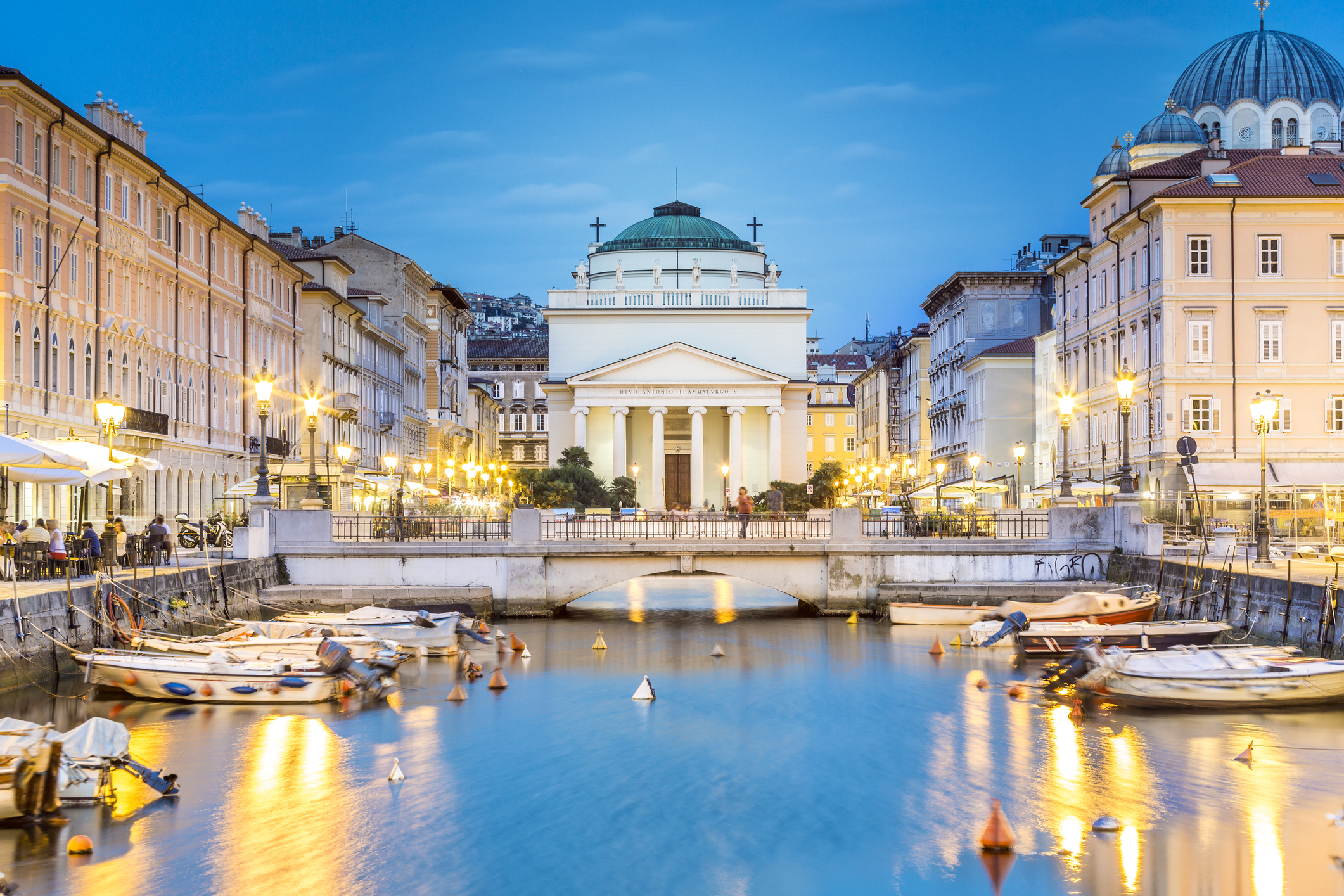 A view of the Grand Canal in Trieste, Italy, with boats docked in the canal and a neoclassical church, Sant&#x27;Antonio Taumaturgo, visible in the background