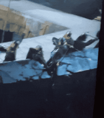 Several figures in medieval-style armor engage in a choreographed fight scene atop a castle-like structure
