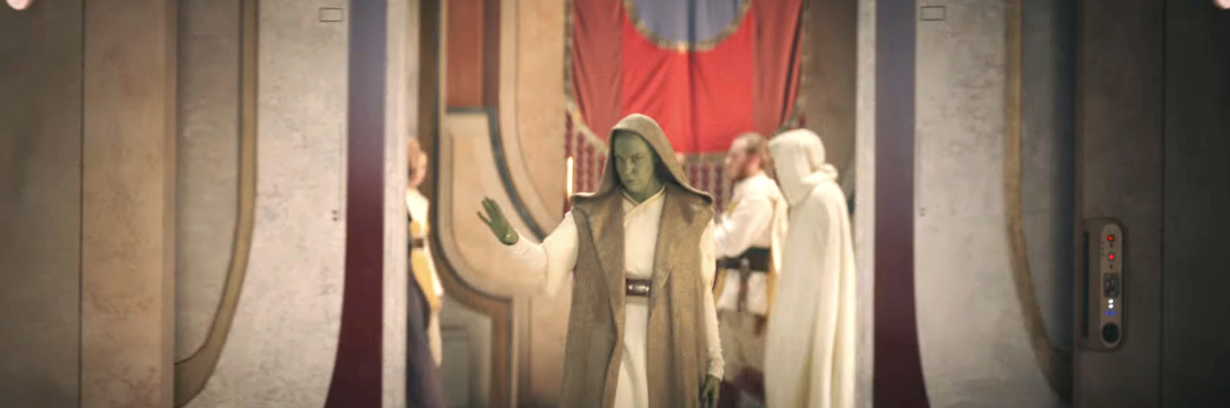 Ahsoka Tano in a hooded robe steps into a room, with others in white robes in the background