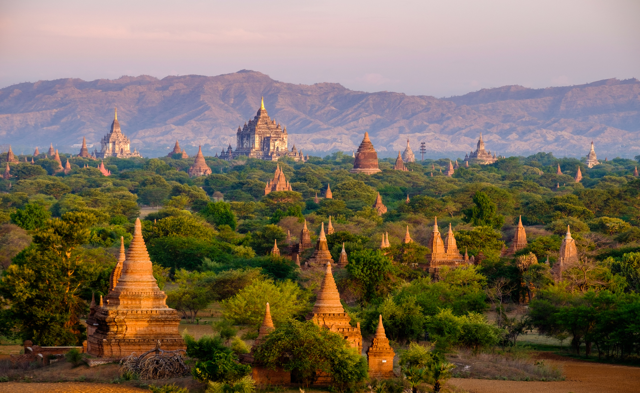 A scenic view of numerous ancient temples and pagodas amidst a lush green landscape with distant mountains in the background