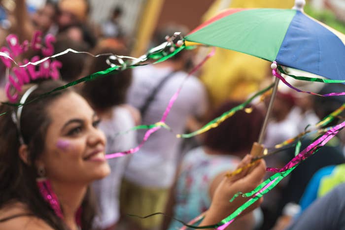 A woman smiles while holding a colorful umbrella adorned with streamers in a festive and crowded street setting