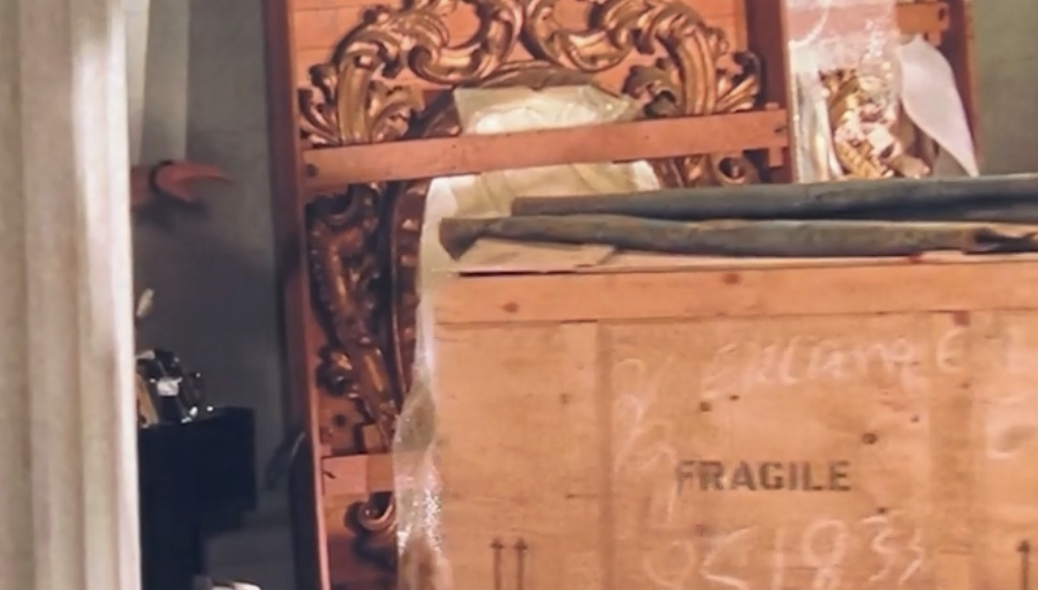 An ornate wooden frame and a large wooden crate labeled "FRAGILE" are shown in a storage area. Other furniture and objects are partially visible in the background