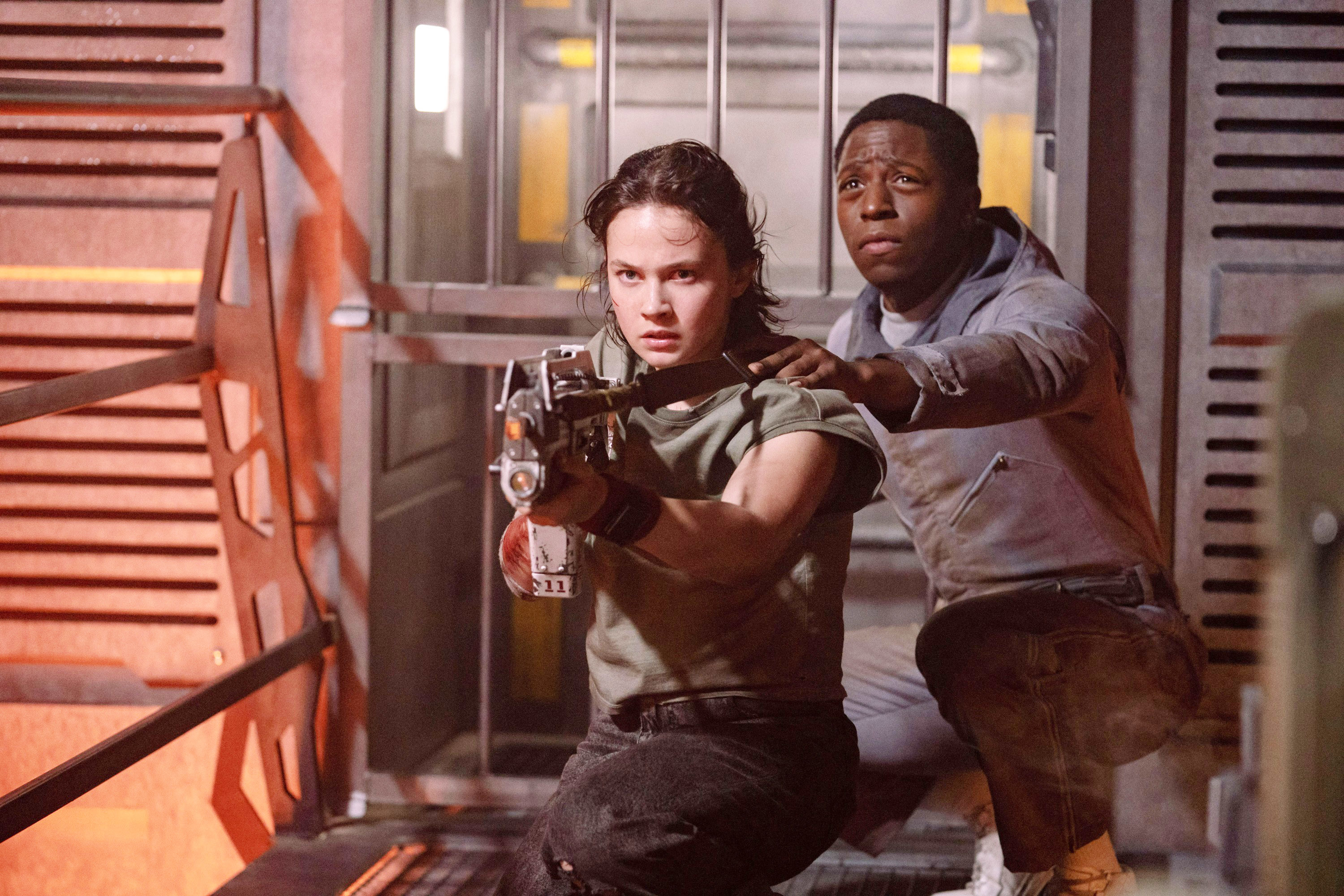Cailee Spaeny aiming a weapon as she crouched down to the ground alongside David Jonsson in a tense fight scene