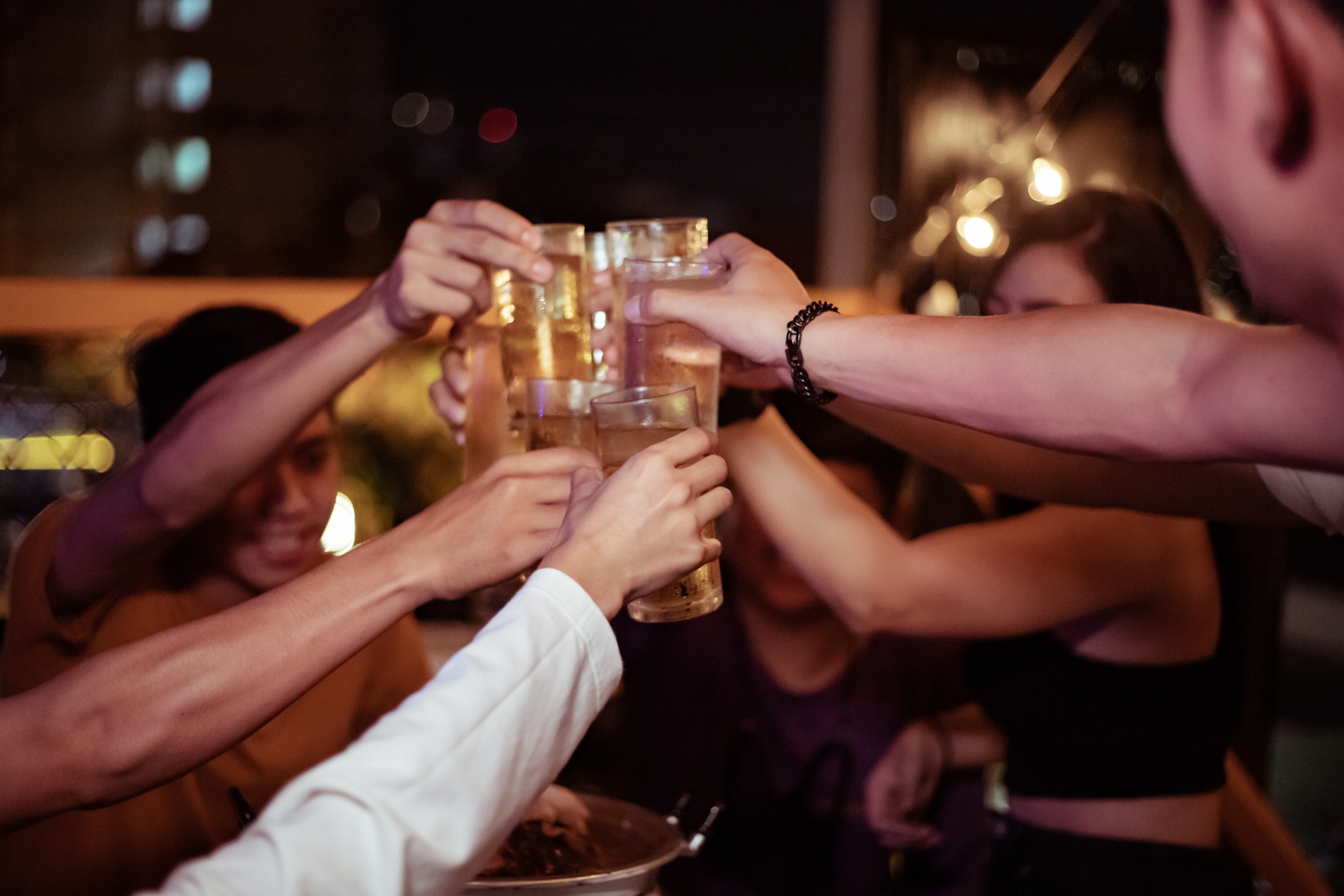 A group of people cheerfully clinking their glasses together in a toast at an outdoor evening gathering. Names of persons unknown