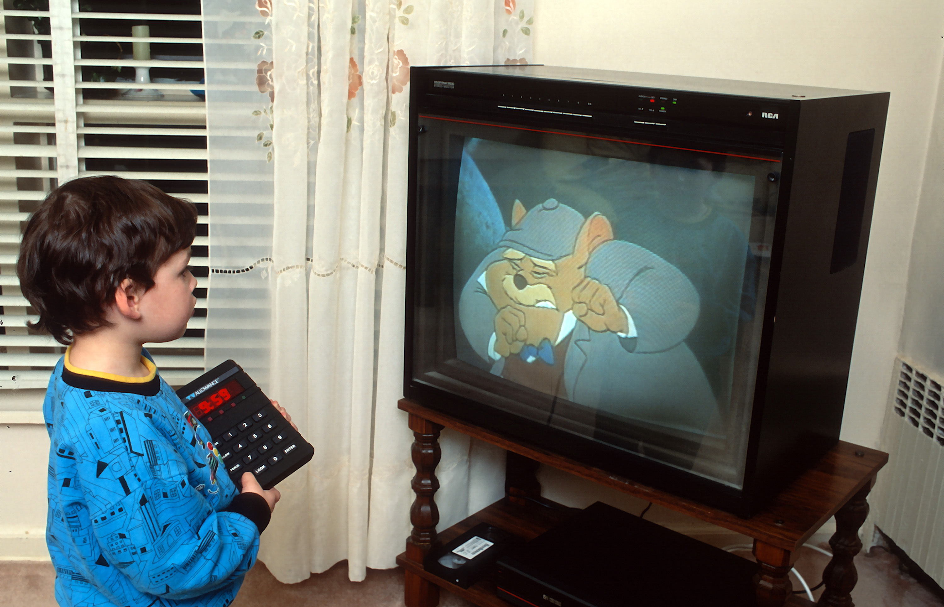 A child wearing a blue shirt watches an animated detective character on an old television while holding a remote control