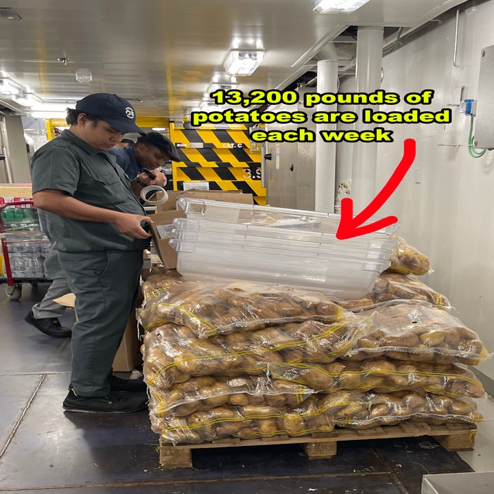 Two people load large plastic containers onto a pallet of potato sacks in a ship's kitchen. Text reads, "13,200 pounds of potatoes are loaded each week."