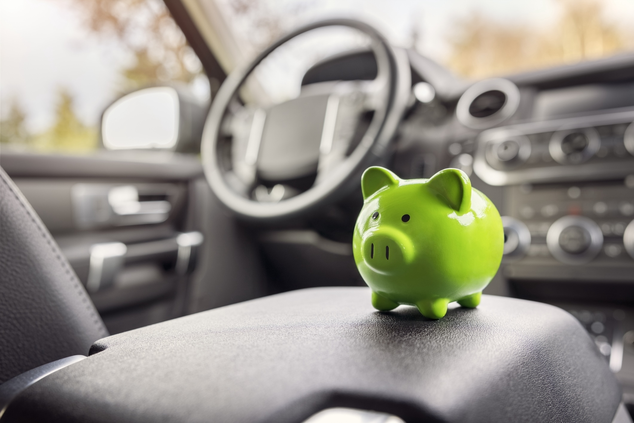 Green piggy bank on car's console, highlighting savings for Work & Money article. Car interior is visible in the background