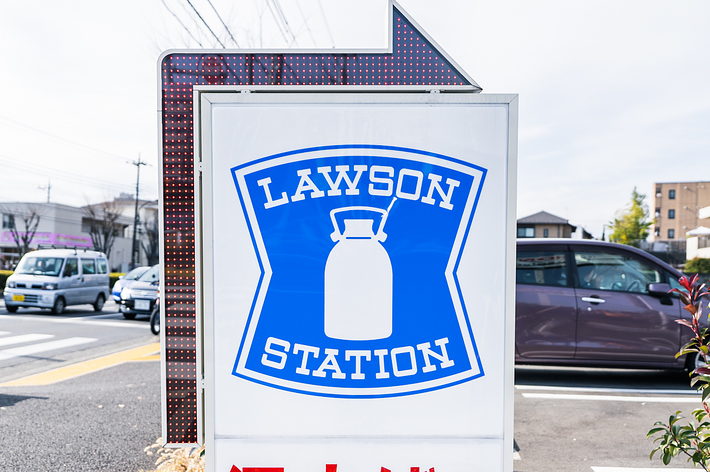 ローソンストアの看板で、日本語で「酒・たばこ」と表示されています。都市の街並みと交通が背景にあります。