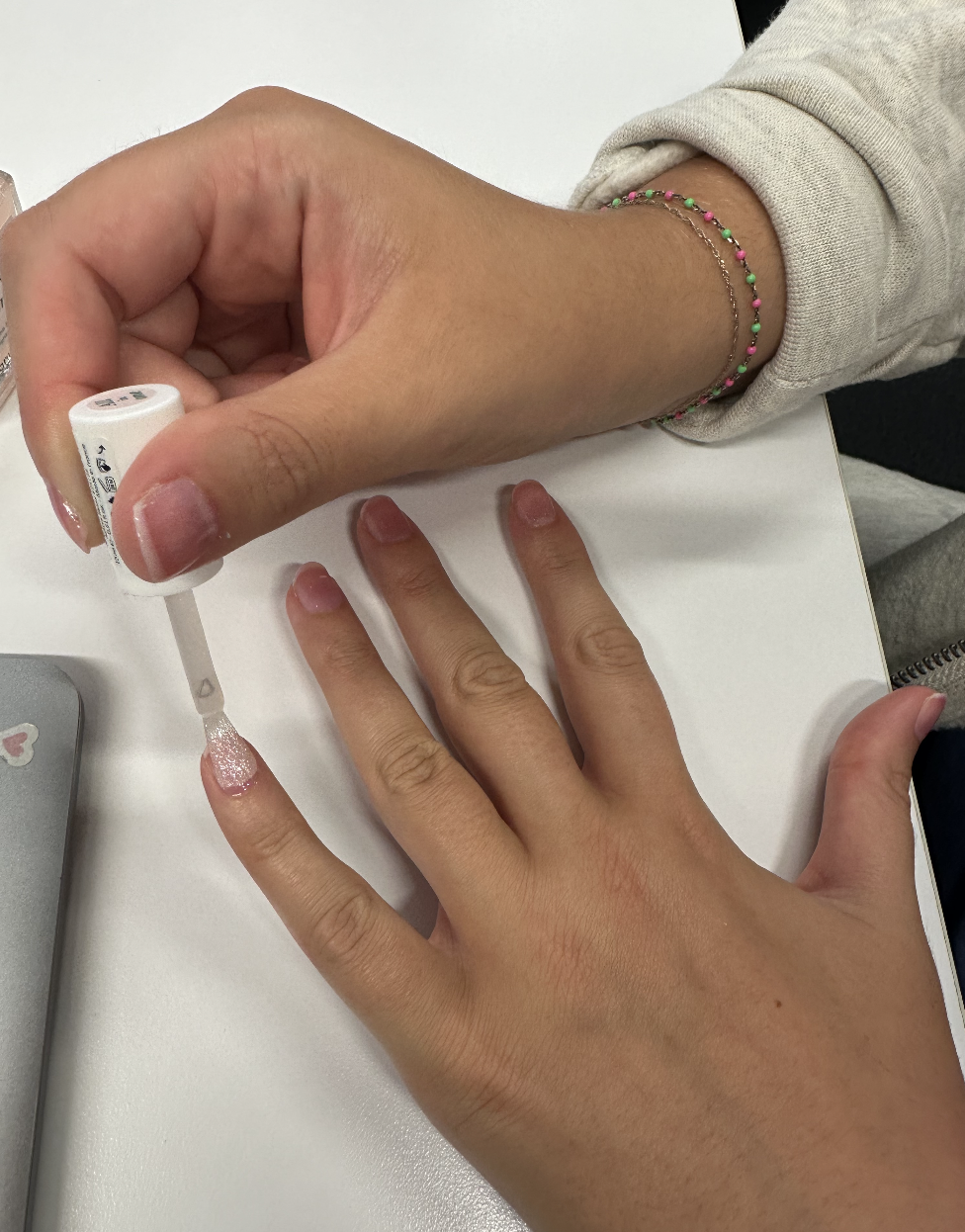 Two hands are visible in the image. One hand is painting the nails of the other with sparkly nail polish