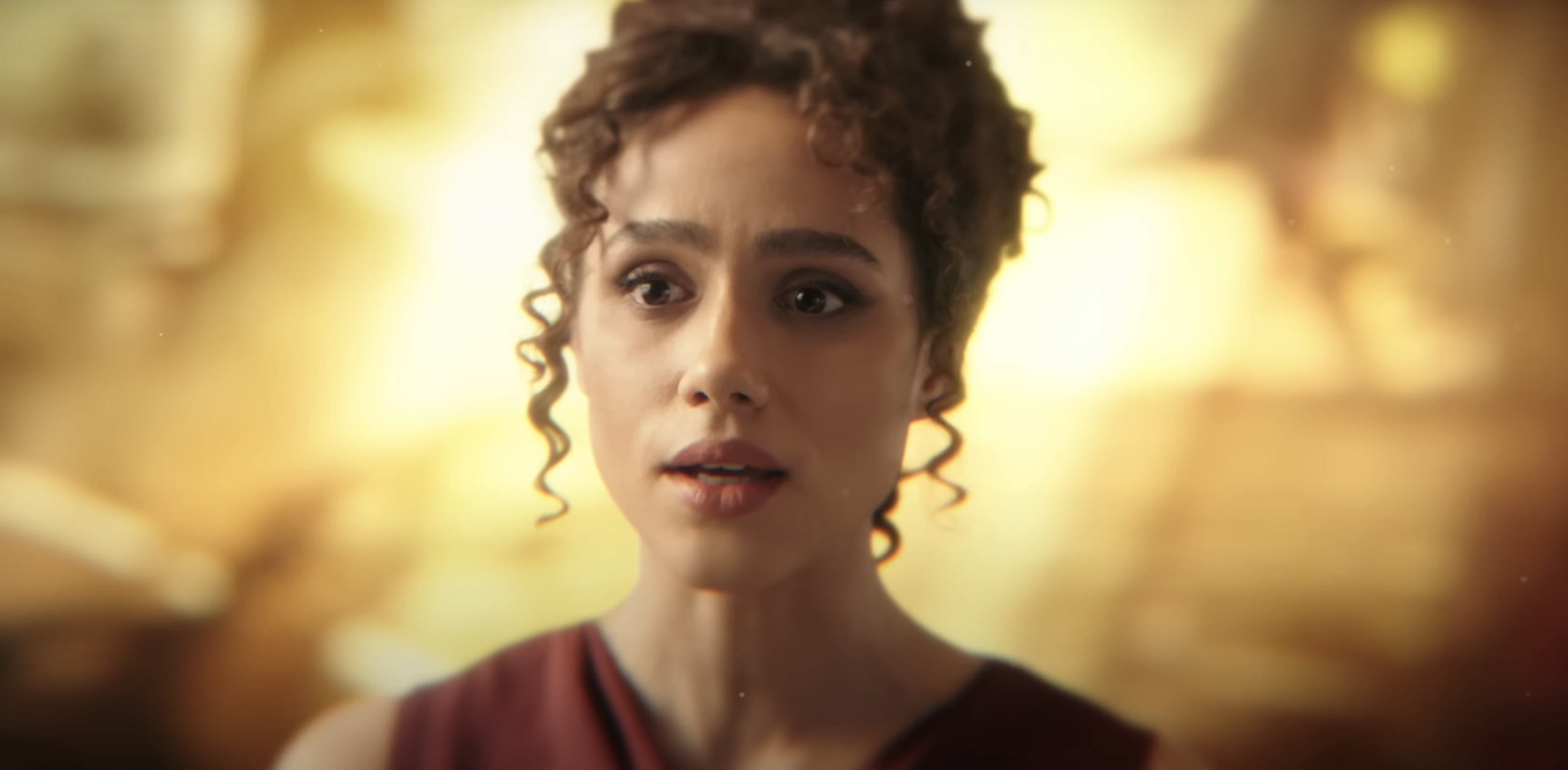 Nathalie Emmanuel as Maya in a dramatic scene looking concerned, wearing a simple, elegant outfit with curly hair pulled back