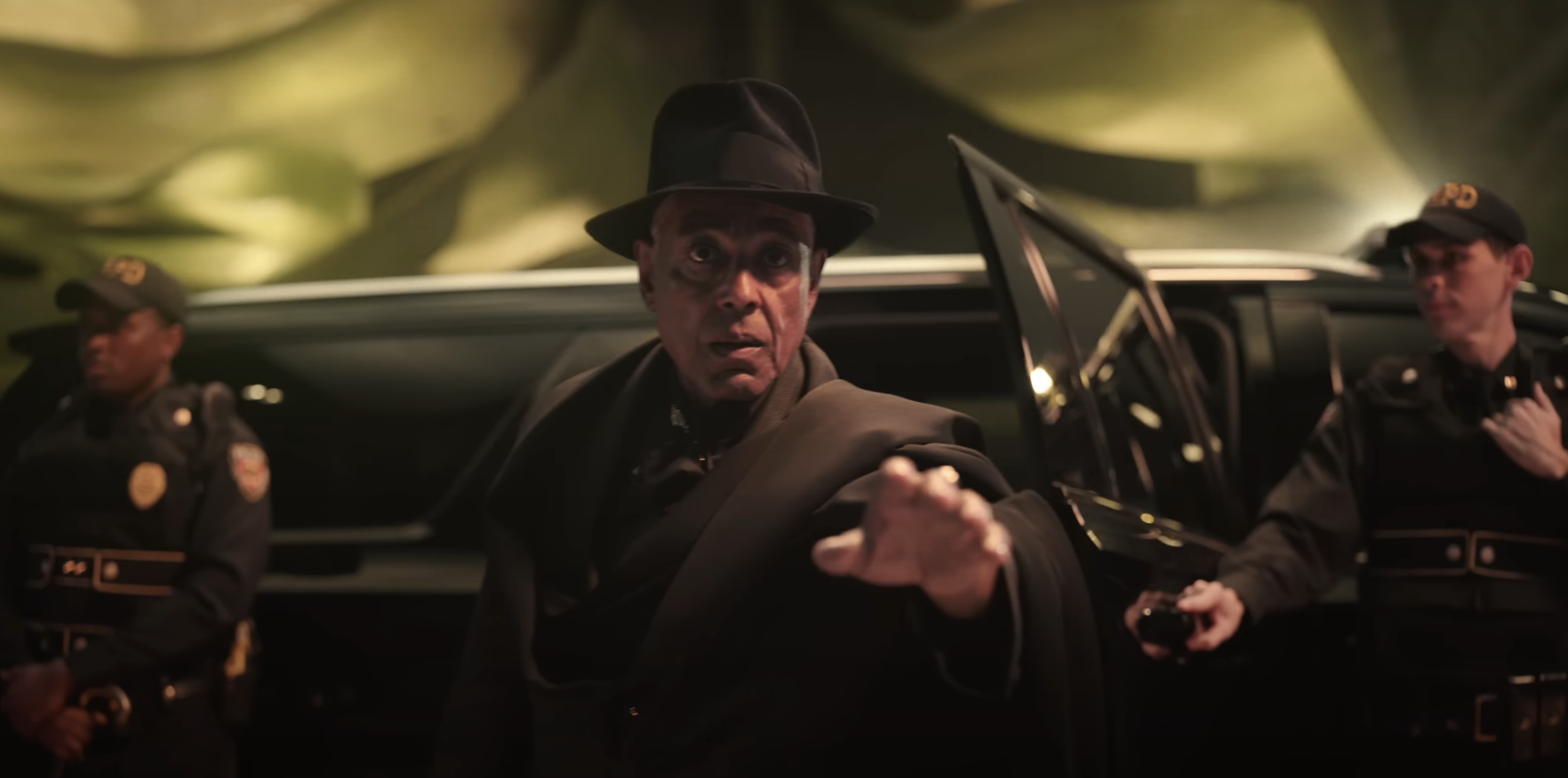 Man in a hat exits a black car with two security guards nearby