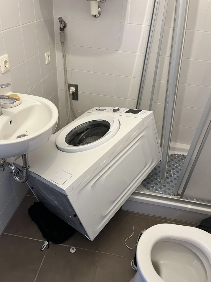 Bathroom with a washing machine flipped onto its side next to a sink, shower, and toilet