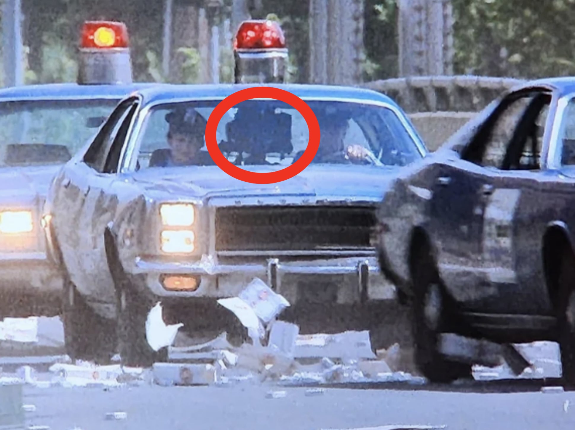 A high-speed police car chase with two cars, one crashing through a debris-strewn street as police vehicles with flashing lights follow closely