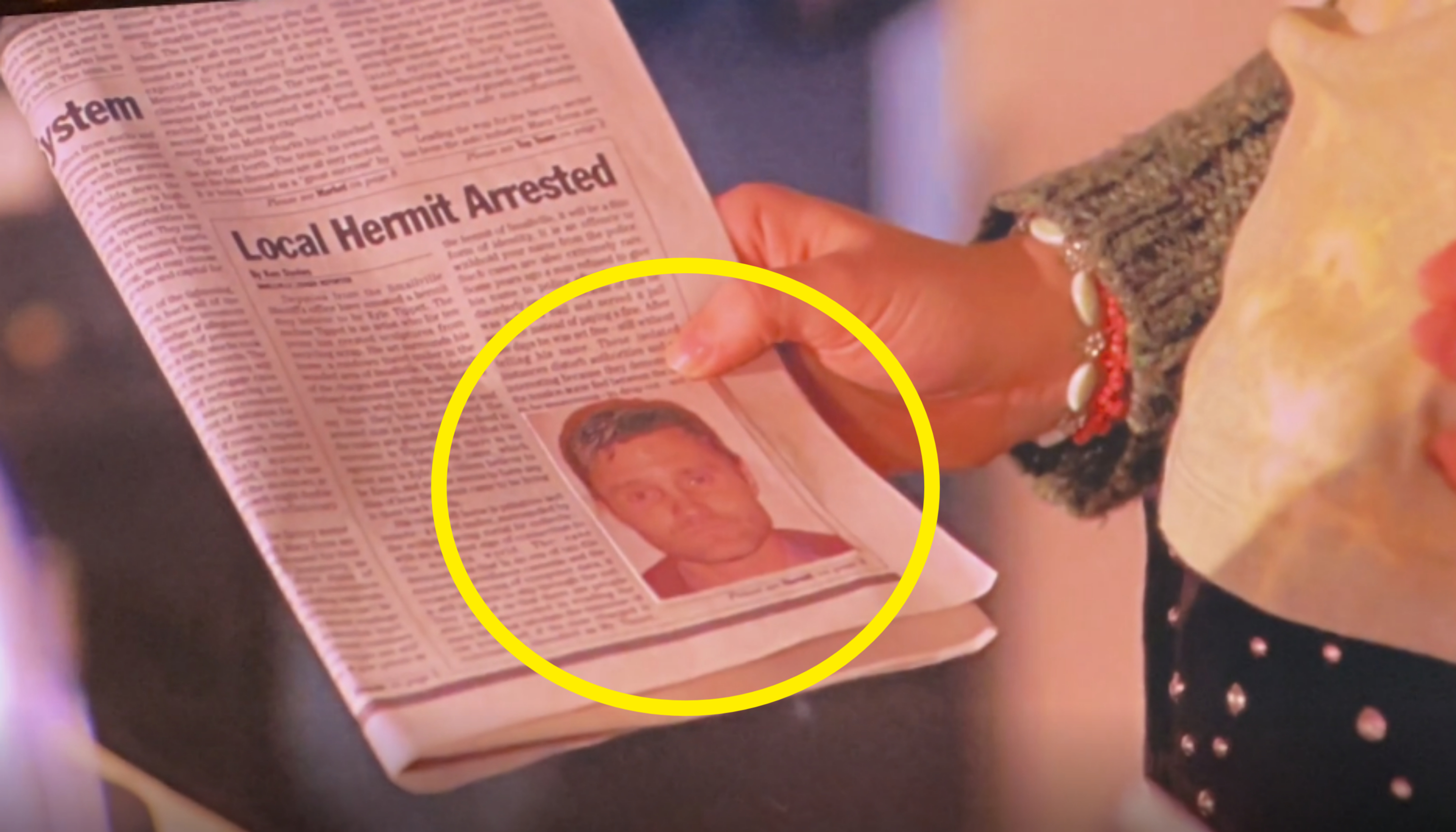 A person holds a newspaper featuring a headline, "Local Hermit Arrested," with an accompanying photo of the arrested individual