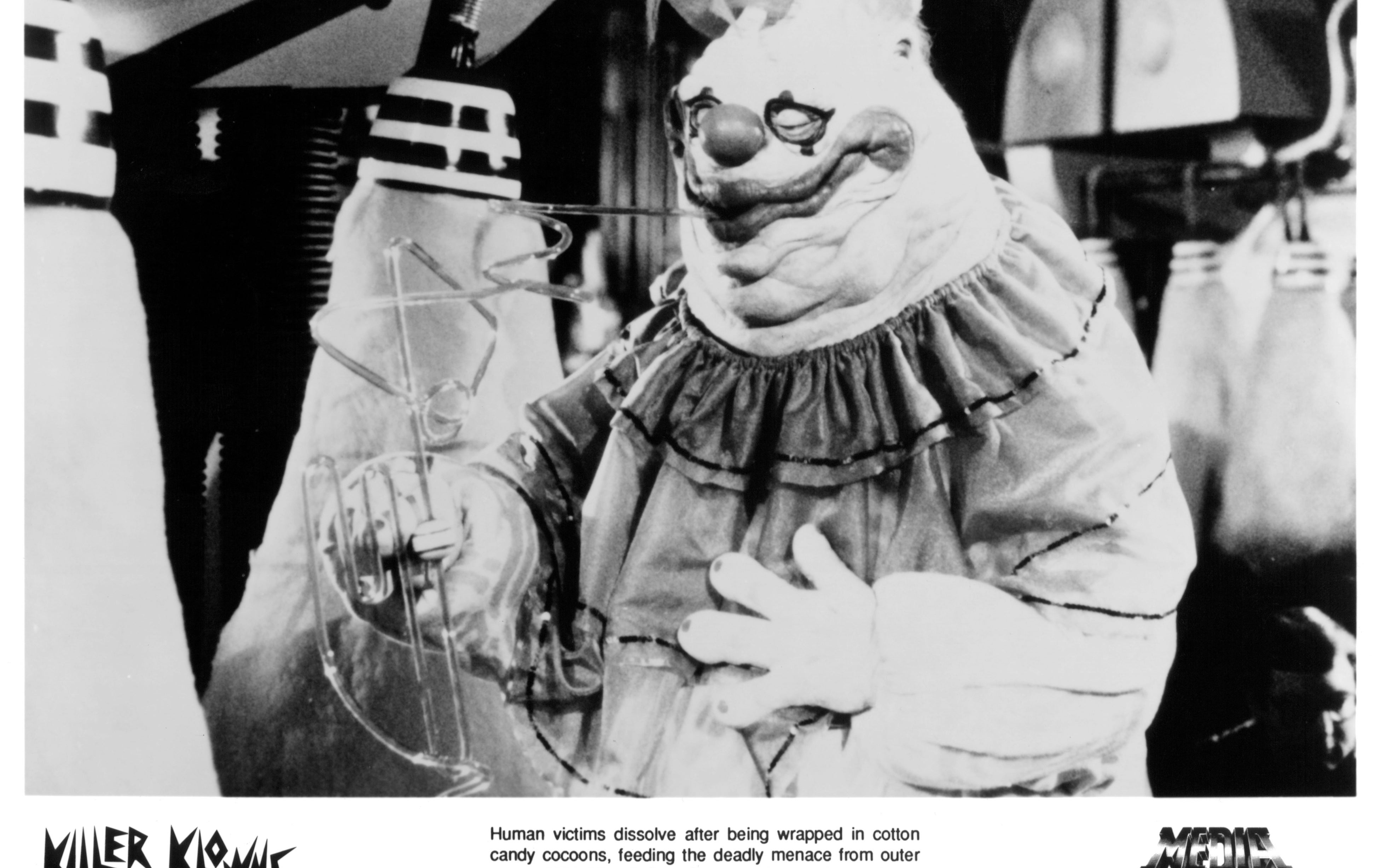 A character from "Killer Klowns from Outer Space" dressed in a clown costume with wrinkled face and ruffled collar stands in a lab setting. Release info below