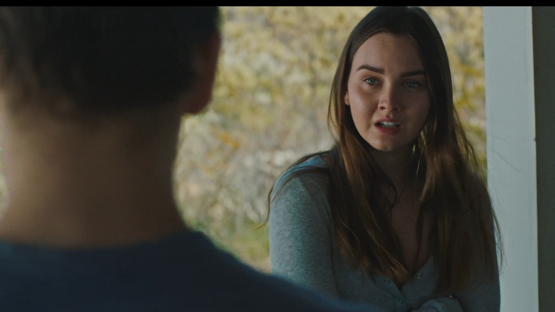 A woman with long hair and a concerned expression looks at a man with his back to the camera