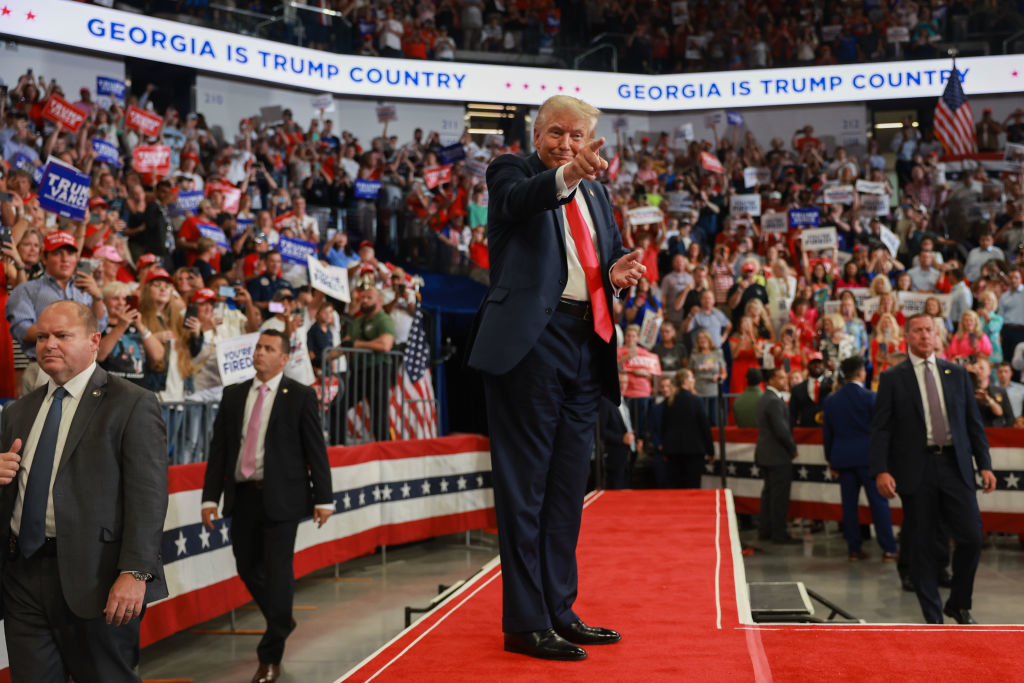 Donald Trump, points and waves to a crowd at a rally