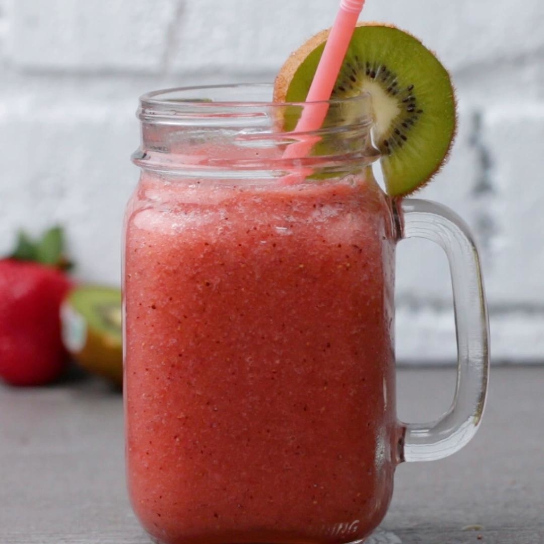 A mason jar filled with a strawberry smoothie, garnished with a slice of kiwi and a pink straw