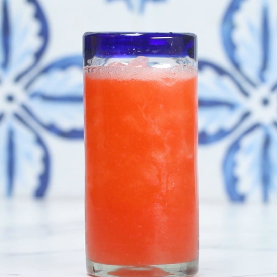A tall glass filled with a bright red slushy drink, against a background with blue floral tile patterns