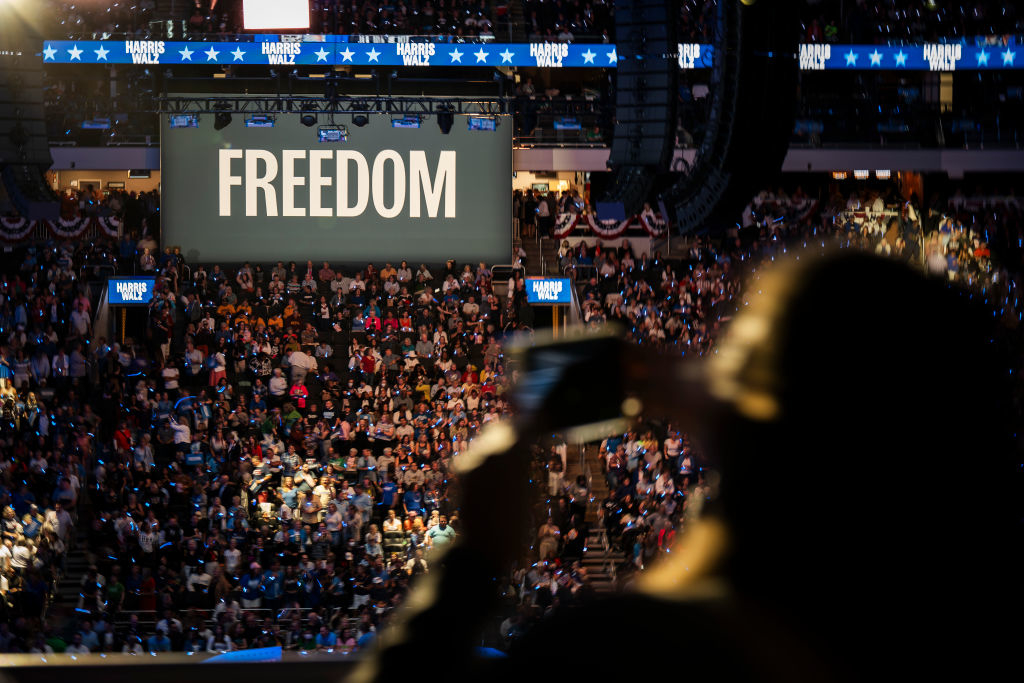 A crowd at an indoor Harris rally with a big screen displaying the word FREEDOM