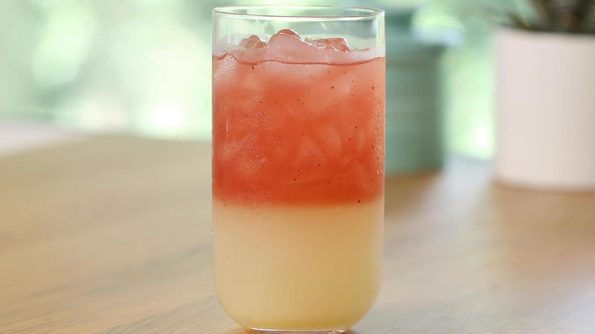 Glass of a colorful layered drink with ice on a wooden surface, blurred background