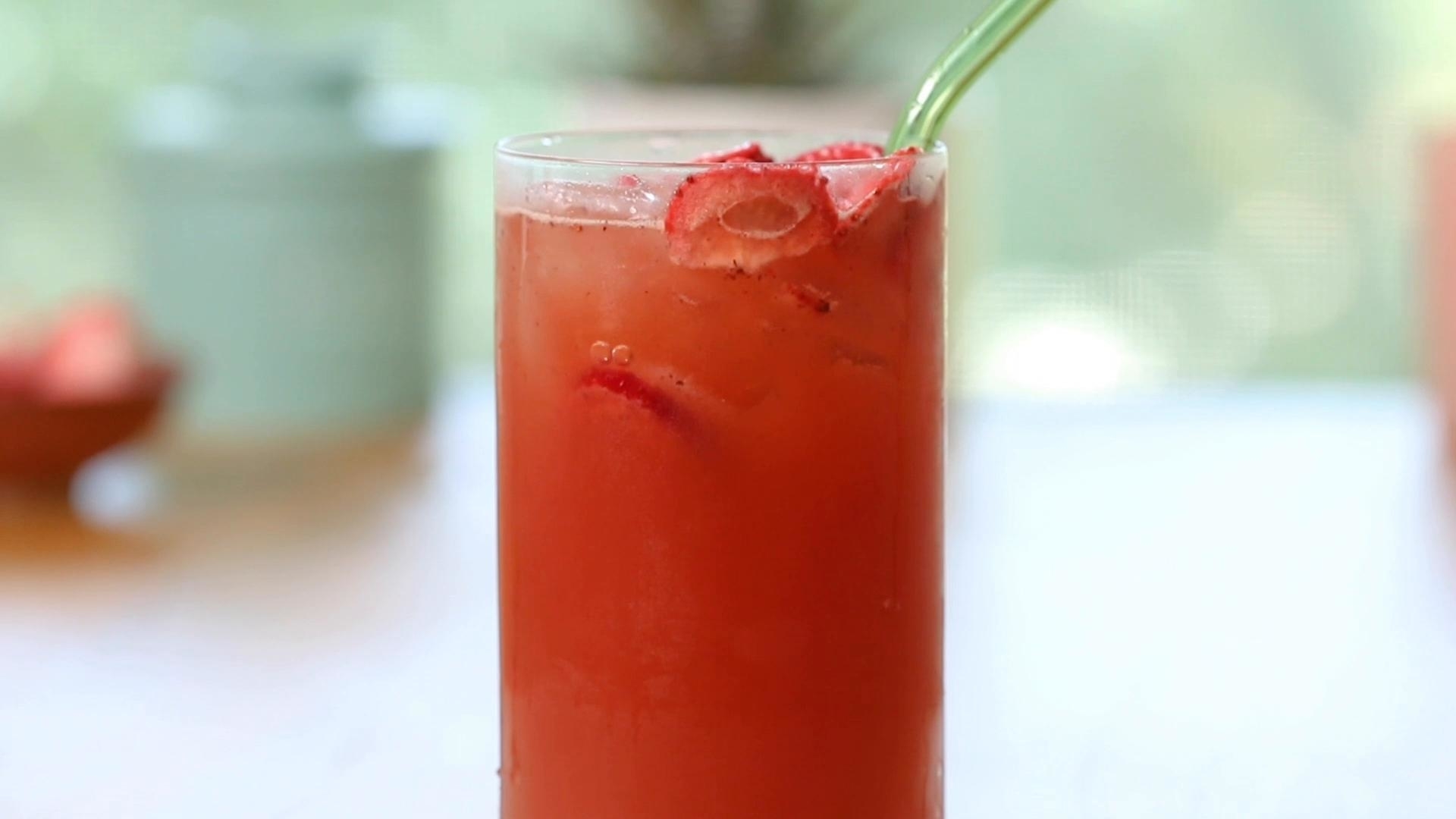 A tall glass of strawberry lemonade with fresh strawberry slices and a green straw