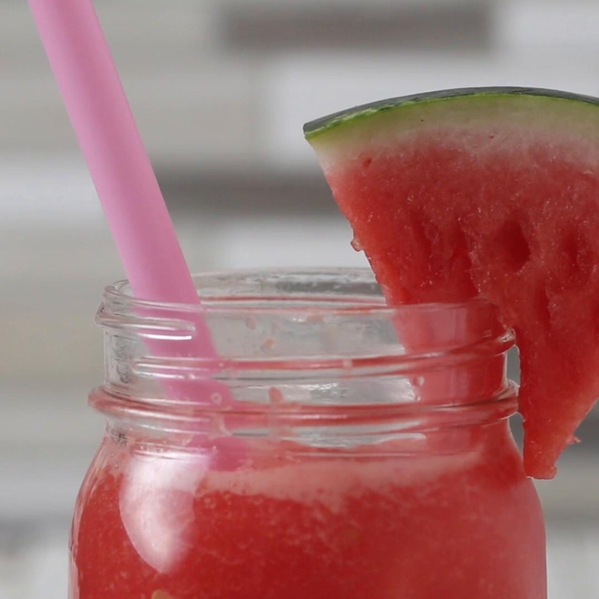 Watermelon smoothie in a jar, garnished with a watermelon slice and a pink straw