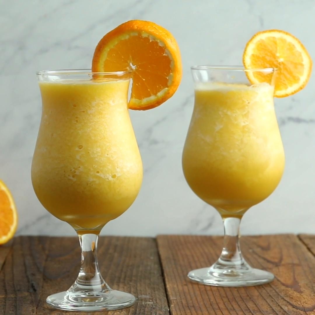 Two glasses of frosty orange smoothies garnished with orange slices on a wooden table