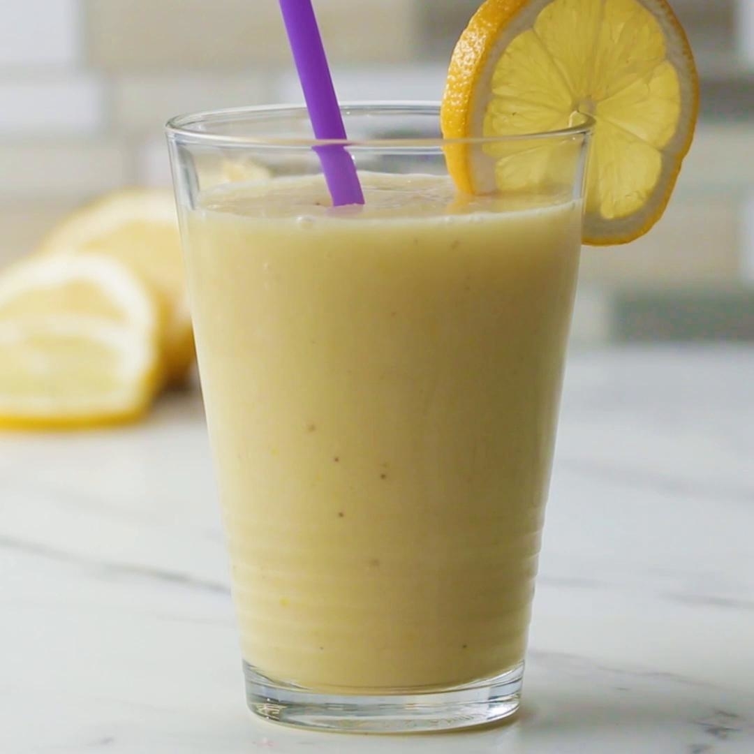 A refreshing glass of lemon smoothie with a purple straw, garnished with a slice of lemon