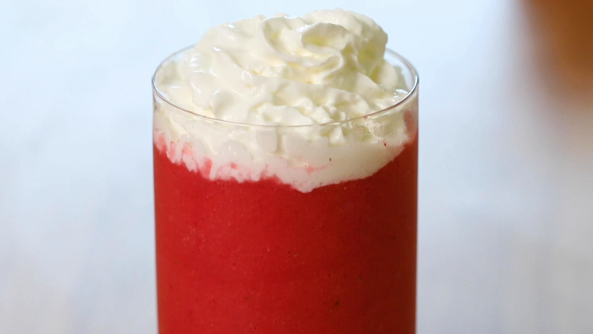 A tall glass filled with a bright red smoothie topped with whipped cream