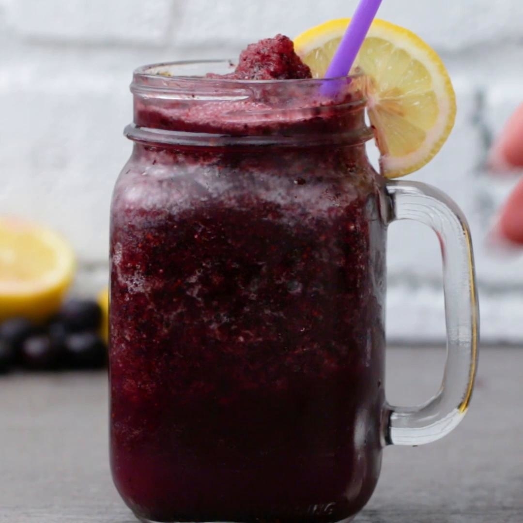 A mason jar filled with a frosty purple slushie, garnished with a slice of lemon and a purple straw