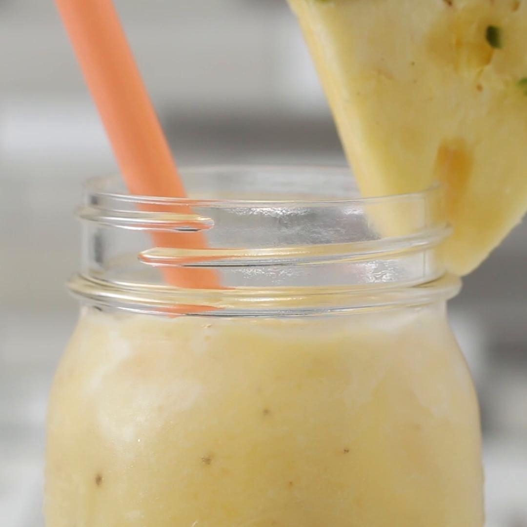 A smoothie in a mason jar with an orange straw and a pineapple wedge on the rim