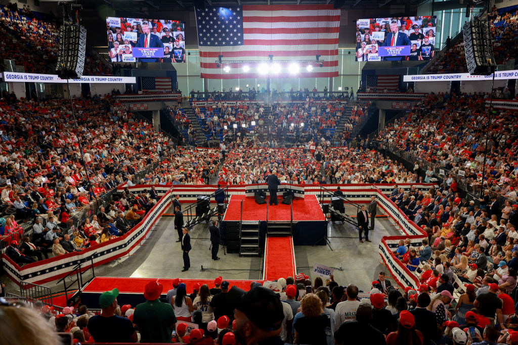 An indoor rally with a large American flag in the background