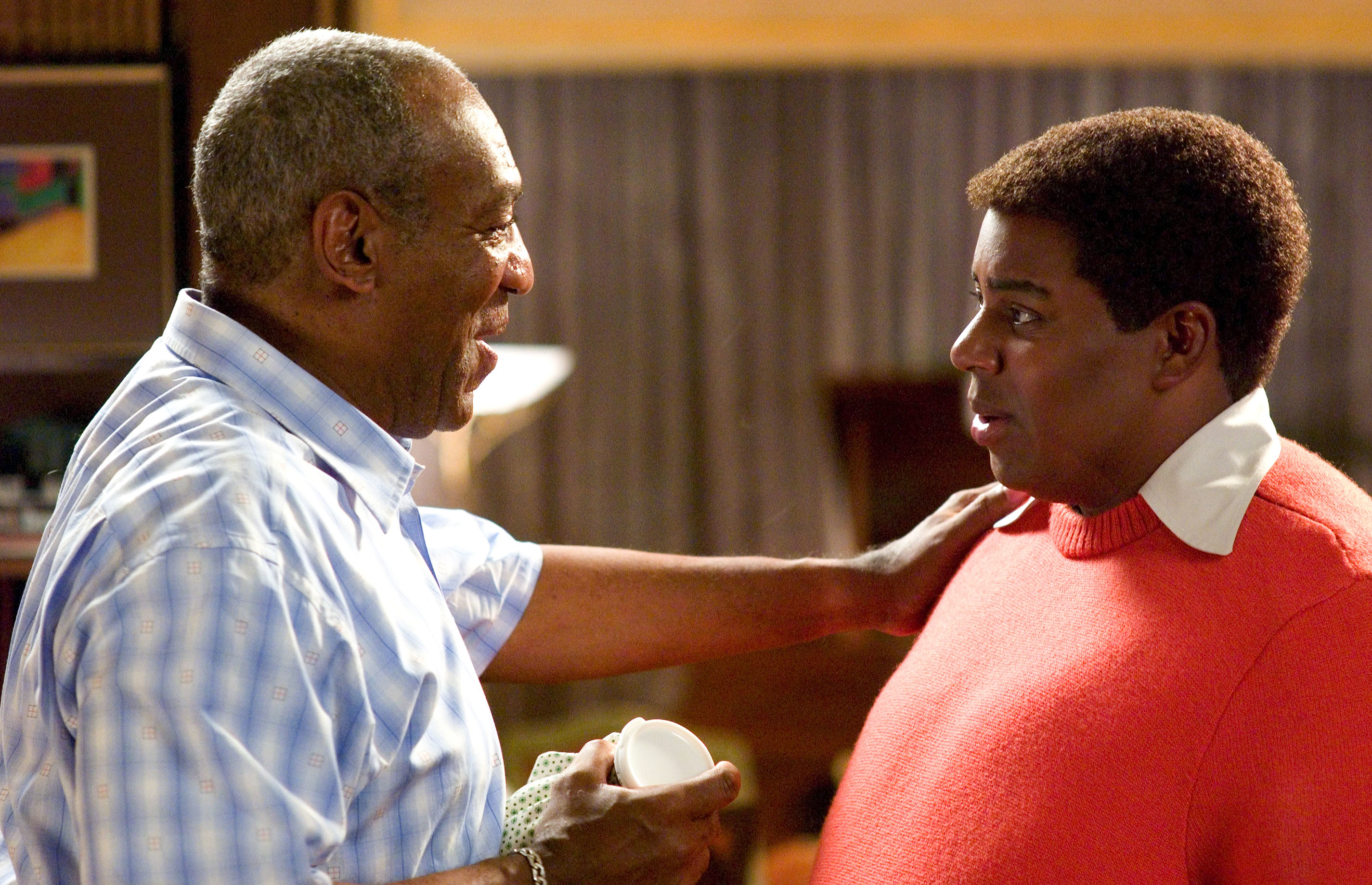 Bill Cosby and Kenan Thompson smile at each other in a warmly lit room, with Thompson's hand on Cosby's shoulder