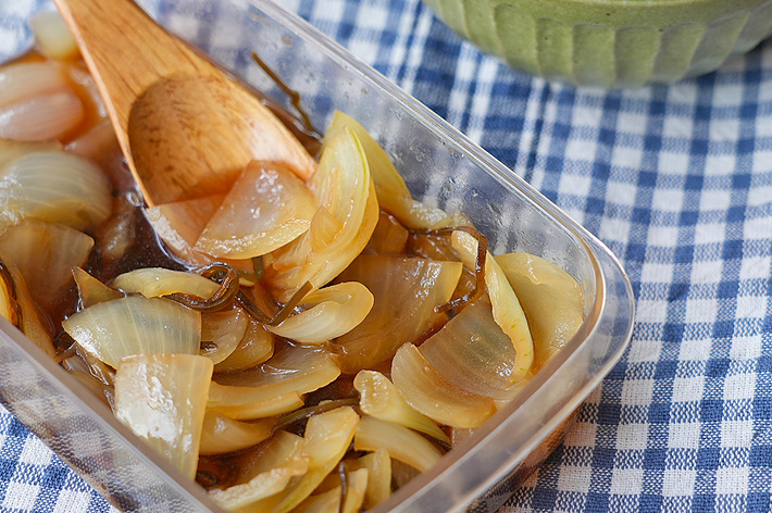 透明な容器に盛り付けられた煮玉ねぎと木製スプーン、背景に白ご飯が写っています。