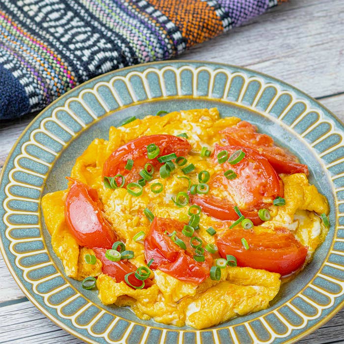 色鮮やかなトマトと卵の炒め物が飾られた皿。皿の横には編み物のクロスが置かれている。